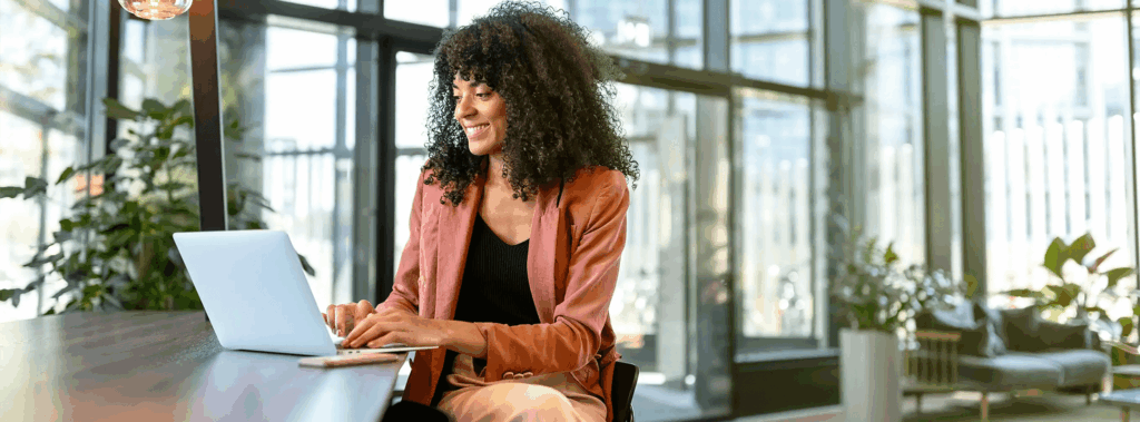 Vrouw kijkt lachend naar haar laptop scherm terwijl ze aan een hoge tafel zit