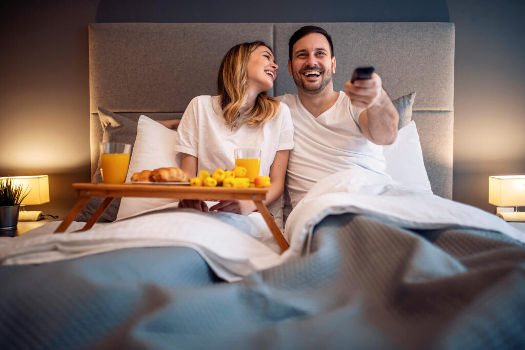 Stel in bed kijkt tijdens ontbijt lachend naar de tv