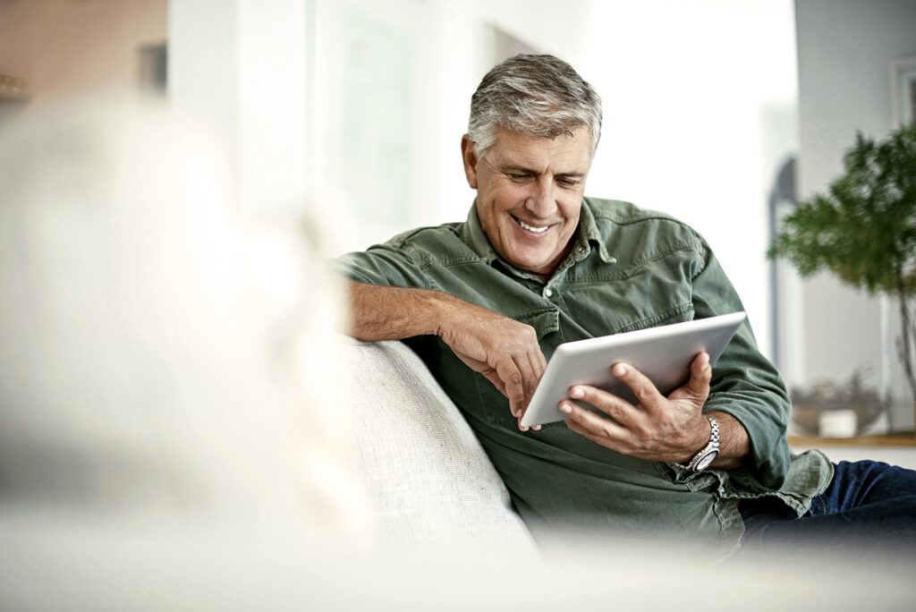 Man zit op de bank lachend naar zijn tablet te kijken