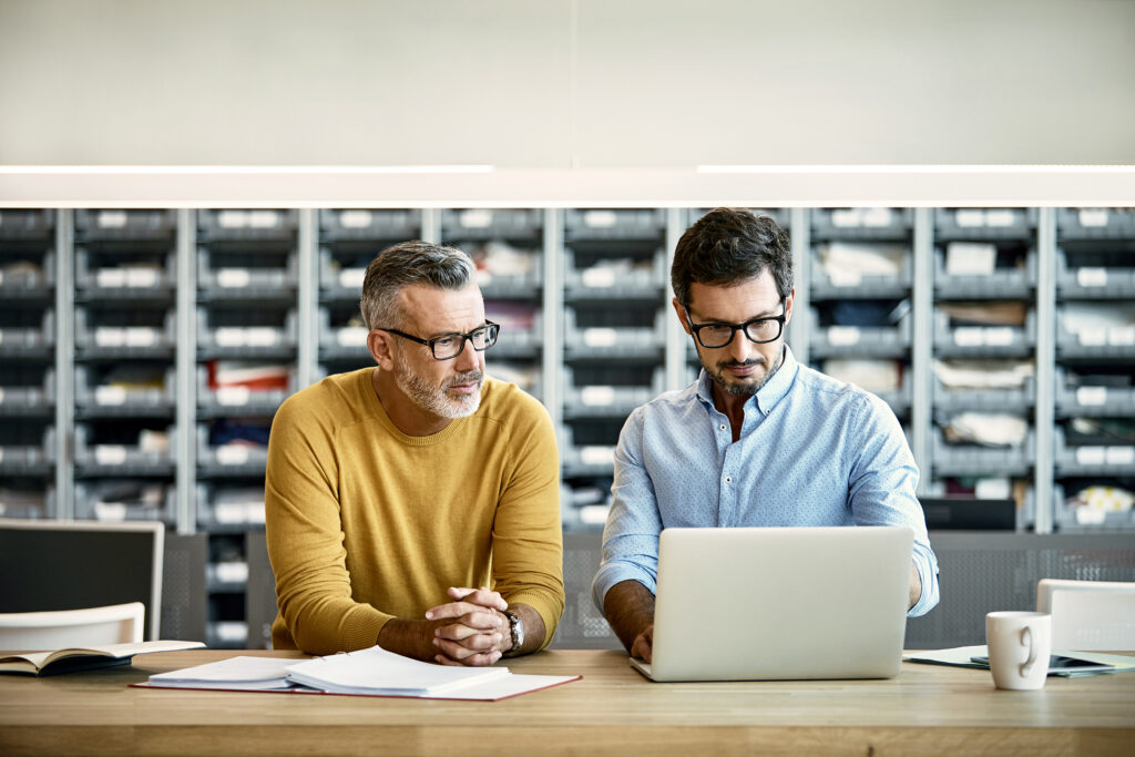 Twee mannen zitten aan een bureau en kijken naar een laptop