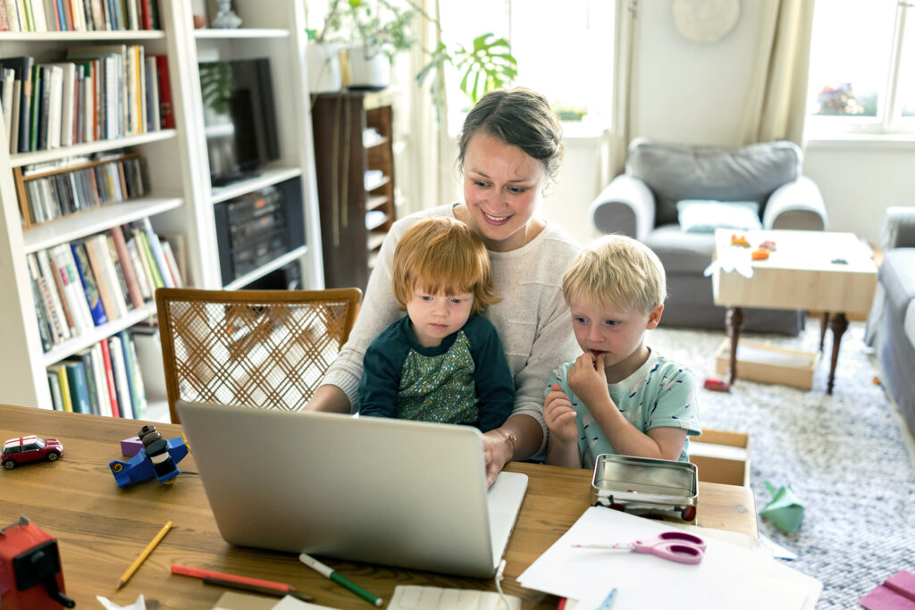 Vrouw kijkt met zoontjes naar laptop scherm terwijl ze aan tafel zitten